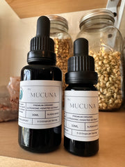 Two Mucuna dropper bottles on a wooden surface with jars in the background.
